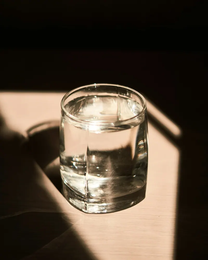 Copo de vidro com água sobre uma mesa, atravessado por um feixe de luz quente.