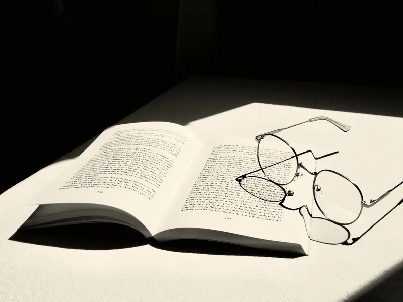 Óculos de leitura sobre um livro aberto, sob luz lateral intensa.
